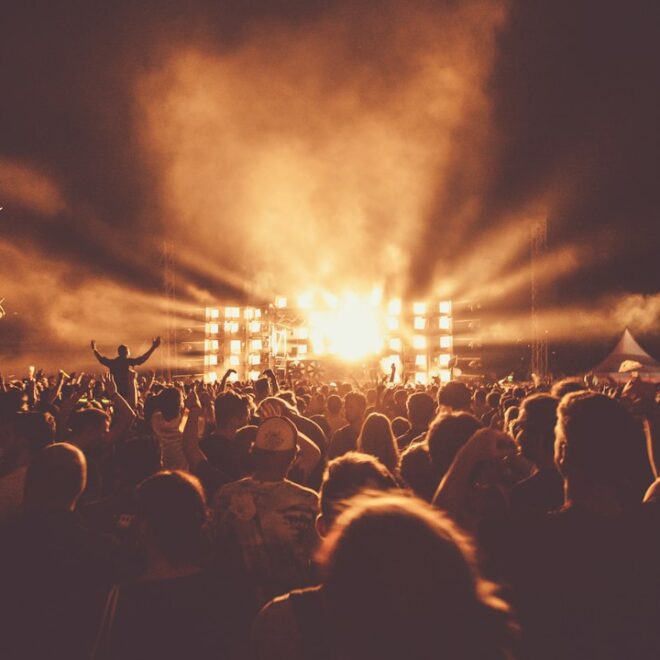 Publikum mit erhobenen Händen und Bühnenlicht bei einem lauten Konzert